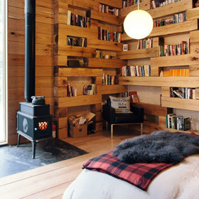 Mezery mezi jednotlivými kládami vytvářejí jakési police, které jsou plné knih.