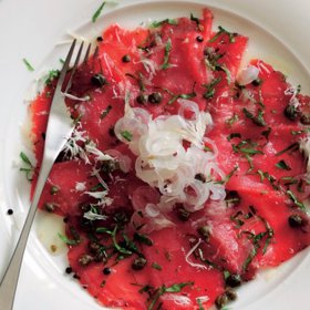 Hovězí carpaccio s kapari

Suroviny:

250 g hovězí svíčkové
mořská sůl a drcený černý pepř
1 lžíce olivového oleje
50 g kaparů v soli
4 nakládané cibulky, na tenká kolečka
3 hrsti nasekané hladkolisté petrželky
extra panenský olivový olej na zakapání
jemně strouhaný parmazán, k podávání

Postup:

Maso posypte solí a pepřem, zabalte do plastové fólie.

Svíčkovou dejte na hodinu do mrazáku, nebo na tak dlouho, aby skoro zmrzla (bude se lépe krájet na opravdu papírově tenká kolečka; nebojte se, velmi rychle roztají). Olej zahřejte na pánvi, vsypte kapary a 3–4 minuty je opékejte dokřupava. Osušte na ubrousku a nechte zchladnout.

Vybalte maso a nakrájejte ho velmi ostrým nožem na teninké plátky. Na čtyři talíře naaranžujte maso, opečené kapary, cibulku a petrželku. Zakapejte olivovým olejem, posypte parmazánem a ihned podávejte.
