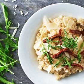 Rizoto se sýrem a sušenými rajčaty
Suroviny
200 g rýže Arborio Italiamo
sýr Grana Padano Lovilio
50 g cibule
olivový olej Luccese
100 ml suchého bílého vína
mořská sůl v mlýnku Kaniaasi
500 ml drůbežího vývaru
30 g másla Pilos
50 g sušených rajčat Italiamo
čerstvá bazalka na ozdobení
100 g čerstvé rukoly
Postup:
Najemno nakrájenou cibuli necháme na olivovém oleji zesklovatět (v mírně rozpáleném hrnci). Přidáme neomytou rýži, kterou restujeme asi minutu, a podlijeme suchým bílým vínem. Necháme chvíli povařit, aby se víno zredukovalo. Osolíme a postupně podléváme vývarem tak, aby byla rýže jen lehce zalitá. Vaříme „al dente“ (tzn. ne úplně doměkka) 18–20 minut na mírném ohni. Rýži zjemníme studeným máslem, dochutíme nastrouhaným sýrem Grana Padano (asi 30 g) a důkladně promícháme. Rizoto by mělo mít krémovou konzistenci, ale nemělo by být vodové.
Rizoto servírujeme v hlubokém talíři. Ozdobíme kousky sušených rajčat, omytou čerstvou bazalkou a rukolou. Posypeme hoblinkami sýra Grana Padano a pokapeme olivovým olejem.