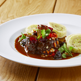 Jelení Ossobuco s pivní omáčkou, bramborovými knedlíky s perníkem, brusinkami a jeřabinami podle šéfkuchaře Lukáše Holého

Suroviny:

Jelení Ossobuco
4 plátky jeleních kolínek 
olivový olej
drcený jalovec 
pepř, sůl

Pivní omáčka
125 g másla
8 šalotek
250 g směsi kořenové zeleniny
80 g cukru
výpek z masa
0,5 l černého piva OSSEGG
100 ml masového či zeleninového vývaru
2 stroužky česneku
4 lžičky tymiánu
2 lžičky rozmarýnu
pepř, sůl

Bramborové knedlíky s perníkem
700 g vařených brambor
200 g hrubé mouky
1 vejce
sůl
100 g perníku na strouhání
50 ml slunečnicového oleje

Brusinky
100 g sušených brusinek
100 ml červeného vína
30 g cukru
hvězdička badiánu
celá skořice

Jeřabiny
jeřabiny v sladkokyselém nálevu
pivovice Svach

Máslová kořenová zelenina
200 g kořenové zeleniny (mrkev, celer, petržel)
olivový olej

Postup:

Jelení Ossobuco: vytvoříme marinádu ze směsi koření, pepře, soli, drceného jalovce a oleje. Směs pečlivě vmasírujme do masa a necháme marinovat alespoň 12 hodin. Pro podávání maso zprudka opečeme na oleji na rozehřáté pánvi. 

Pivní omáčka: kořenovou zeleninu nakrájíme na kostičky, šalotku nakrájíme najemno. Na másle opečeme zeleninu, přidáme šalotku. Když je vše dozlatova opečené, přidáme výpek z masa, poté zalijeme černým pivem a vývarem, přidáme drcený česnek a bylinky a vaříme na mírném ohni alespoň 20 minut.
Do připraveného základu omáčky vložíme na pánvi opečené maso a při nízké teplotě dusíme doměkka. Potom maso vyjmeme a pivní omáčku propasírujeme a dále sváříme na požadovanou hustotu. Když máme svařeno, přidáme vychlazené máslo, sundáme ze sporáku a máslo zašleháme. Hotovou pivní omáčku ještě dochutíme solí.

Bramborové knedlíky s perníkem: z uvařených brambor, mouky, vejce a soli vypracujeme těsto.  To pak vyválíme do tenkého plátu, potřeme štětcem připravenou směsí oleje a najemno nastrouhaného perníku. Těsto zarolujeme a upravíme do tvaru knedlíku. Knedlíky vaříme v páře 28 minut. Po uvaření knedlíky potřeme máslem nebo sádlem, krájíme a servírujeme

Brusinky: sušené brusinky vaříme ve víně s cukrem a kořením na mírném ohni alespoň 10 min, potom brusinky s kořením scedíme a zbylou šťávu svaříme na polovinu. Nakonec do šťávy vrátíme povařené brusinky.

Jeřabiny: nakládané jeřabiny marinujeme několik dnů v alkoholu.

Máslová kořenová zelenina: zeleninu nakrájíme na malé kostičky a orestujeme na pánvi na másle na zkus a dochutíme solí a pepřem.

Servírování
Plátek ossobuco zdobíme na talíři máslovou kořenovou zeleninou, přidáme brusinky a jeřabiny a spolu s perníkovými knedlíky přelijeme pivní omáčkou. 
