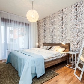 Přírodní prvek se zde promítá nejen do dřevěné podlahy, ale prostřednictví tapety také na zeď. Tlumené odstíny béžové a světle modré a motiv zasněženého stromu navozují v ložnici klidnou atmosféru.