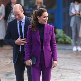 Kate Middleton ve fialovém kalhotovém kostýmku, který zkombinovala s černými lodičkami, černým prošívaným psaníčkem a kruhovými náušnicemi.

Pokud byste si na českých e-shopech chtěla pořídit podobný outfit, jeho celková cena by činila zhruba 16 241 Kč.