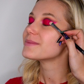 Začněte líčením očí. Na víčko naneste podkladovou bázi a následně vystínujte tmavším (ideálně hnědým) stínem záhyb horního víčka. Pod něj postupně nanášejte světlejší odstíny, abyste vytvořila jemný a přirozený přechod. Poté na víčko naneste červenou rtěnku a zafixujte ji očním stínem v červené barvě. Rtěnku rozestínujte po celém horním víčku až k linii záhybu a jemně ji protáhněte až tak, abyste docílila takzvaného kočičího líčení. 