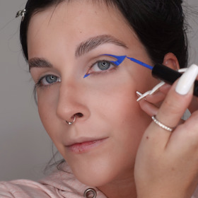 Modrou tekutou linkou nakreslete na víčko grafickou linku. Začněte od vnějšího koutku a veďte ji až do ohybu oka. Pro ozvláštnění vytvořte zobáček linky ve vnitřním koutku, čímž získáte více kočičí tvar oka.