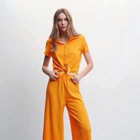 Oranžová v jednom celku. Kalhoty a blůza s vázačkou v pase tvoří vyladěný pár. Kalhoty Mango (599 Kč), košile s uzlem Mango (599 Kč)