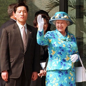 Královna Alžběta II. v rukavicích, které jí pro příležitost návštěvy Jižní Korey v roce 1999 doručil na motorce přímo do paláce manžel Genevieve Andrew Lawson.