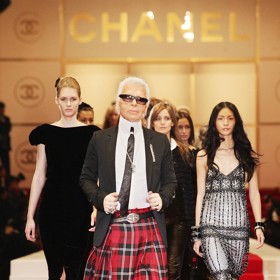 Dlouhou károvanou sukni oblékl i velikán na poli módy, zesnulý návrhář Karl Lagerfeld. Zde například prochází molo se svými modelkami během prezentace kolekce Chanel jaro/léto 2005 v provizorním hledišti v parku Hibiya v centru Tokia.