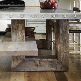 Jídelní stůl kombinuje mohutné kusy kovu a dřeva. Je vybaven šikovnou poličkou, kam lze odložit nádobí těsně před servírováním chodu.