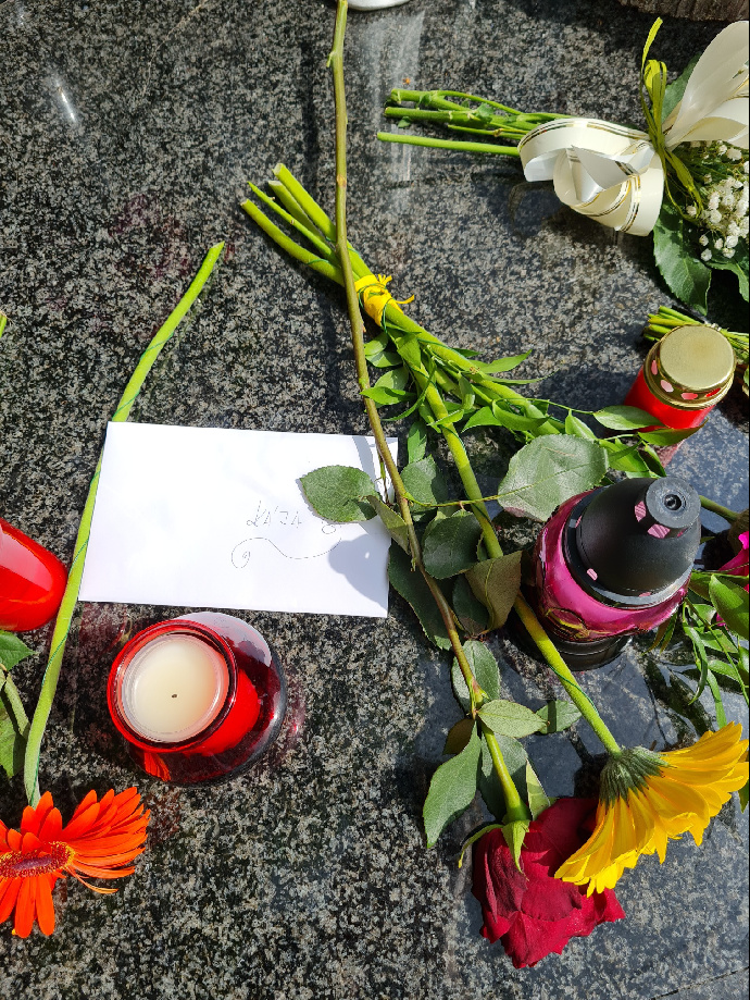 FOTO: Vedle květin a svíček někdo zanechal dopis. Na obálce je zdobným písmem napsáno: Kája. – stránka 267