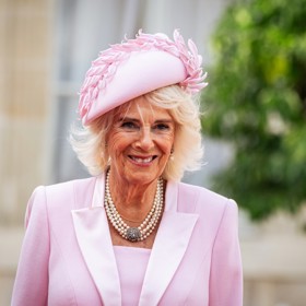 Růžové plášťové šaty doplnil stejně stylový klobouček a také impozantní klenot. Jeden ze šperků, který Camilla nosí nejčastěji, čtyřřadý perlový náhrdelník s diamantovou sponou.