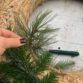 Větvičky postupně klaďte na tělo věnce ze slámy, na které jste si upevnili vázací drátek.