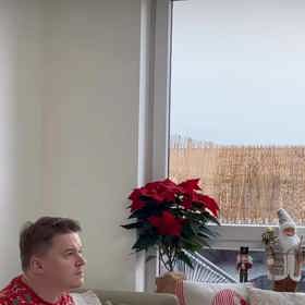 Scenárista Petr Kolečko sedí u televize ve vánočním červeném kompletu.