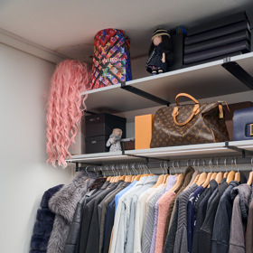 Pohled na levou stranu šatny s ramínky, na kterých visí svetry a košile.