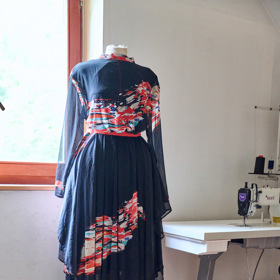 U okna, pěkně na světle, stojí jedna oblečená krejčovská panna.