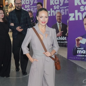 Lucie Vondráčková oblékla krásný šedý overal se zajímavými prvky přepásání v pase i kravatou ve výstřihu. Cestovní brašnu s popruhem  později na focení odložila.