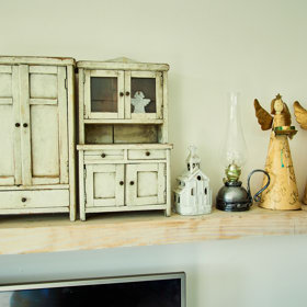 Nad televizí je jednoduchá polička s drobnými dekoracemi a osobními předměty.