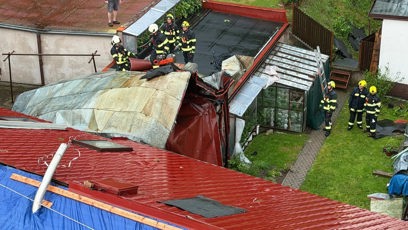FOTO: Pohled ze shora na zničenou střechu rodinného domu a zasahující hasiče s motorovou pilou.