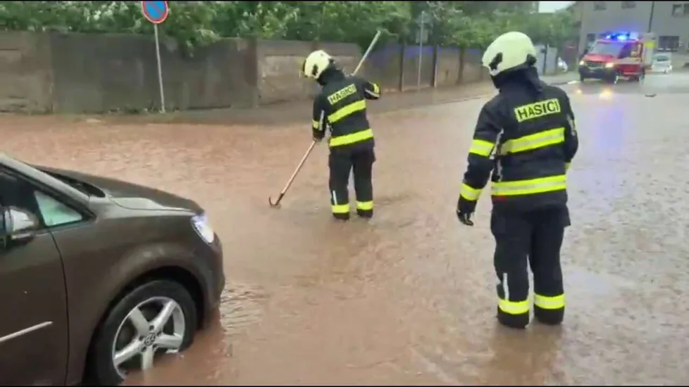FOTO: Hasiči v zatopené ulici čistí kanalizační vpusť, aby bleskové přívaly vody mohly odtékat.