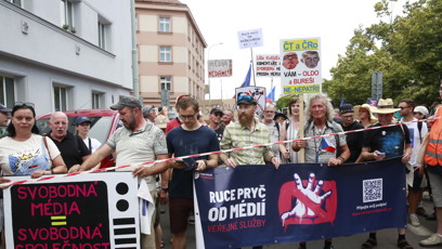FOTO: Demonstranti v čele průvodu drží velký tmavý transparent vyzývající k ochraně veřejné služby.