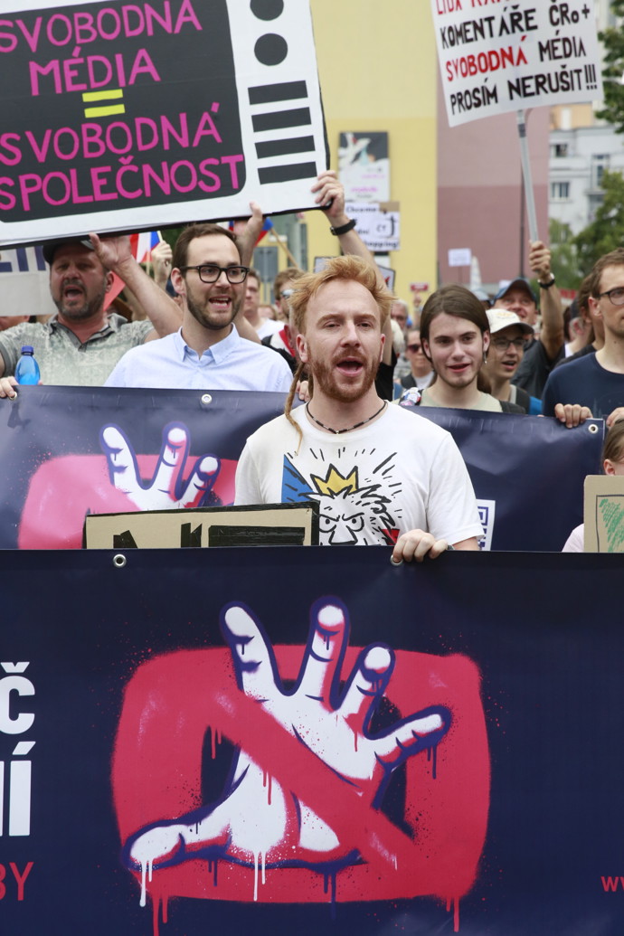 FOTO: Detailní záběr na skupinu účastníků pochodujících s transparenty v předních řadách demonstrace.