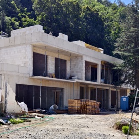 Na staveništi leží stohovací desky a stavební materiál, práce na vile jsou v plném proudu.