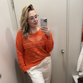 Lehký svetřík syté oranžové barvy z výprodeje Marks& Spencer koupíte za 749 Kč. Bílé kalhoty s madeirou a vázáním na lýtku za 699 Kč.